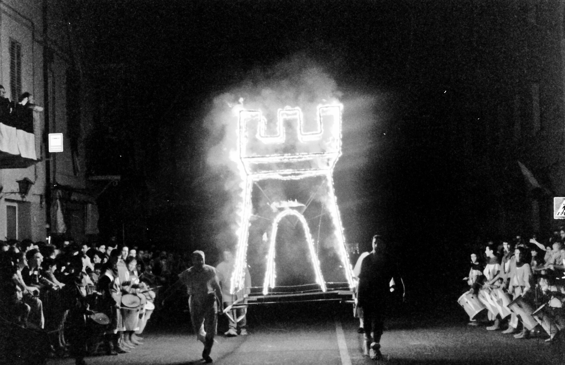Corteo del Rione Pedicino in bianco e nero, con una grande torre illuminata e il pubblico ai lati